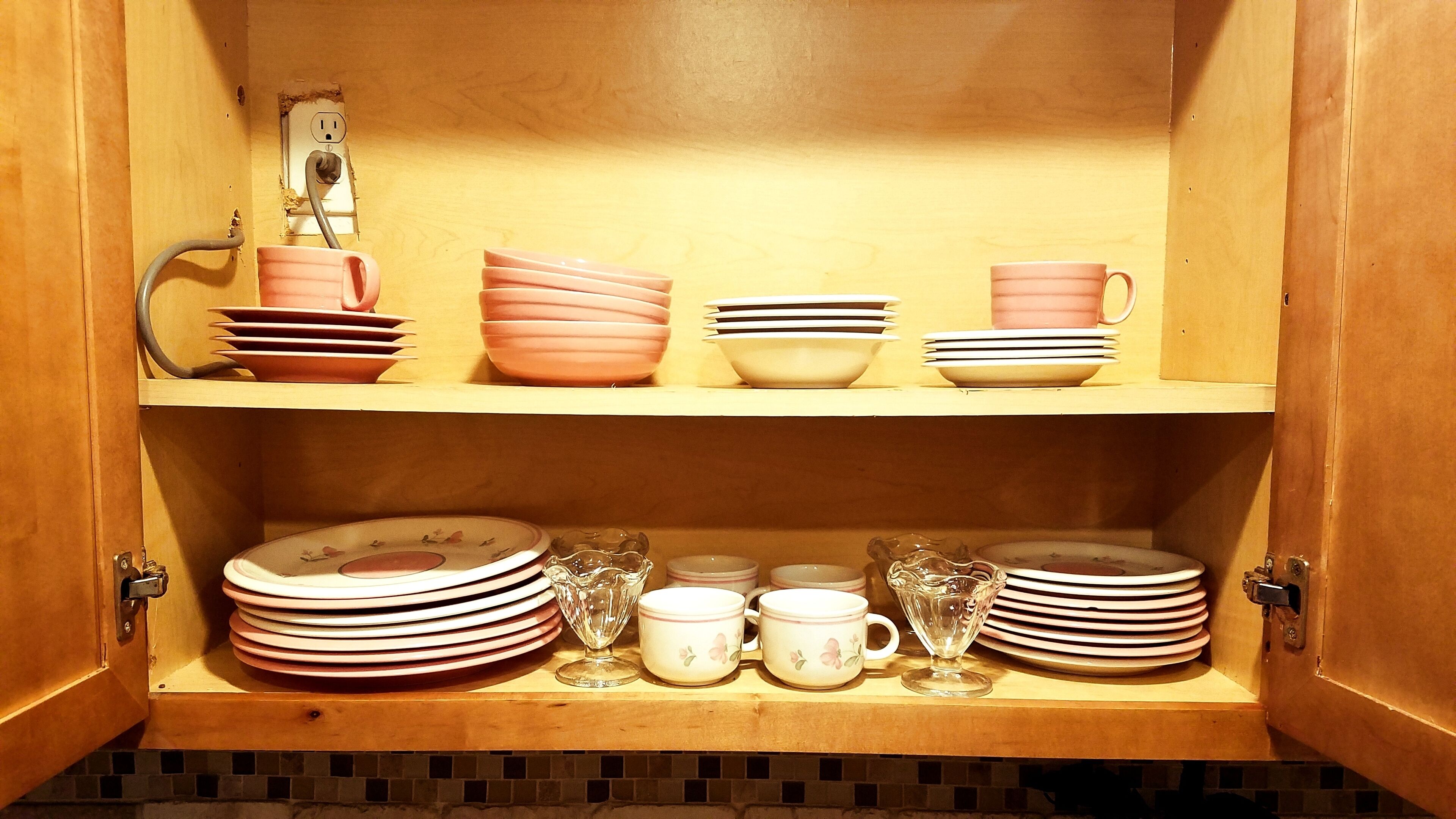 A wooden cabinet with shelves holding plates, bowls, and cups.