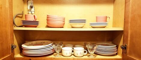 A wooden cabinet with shelves holding plates, bowls, and cups.