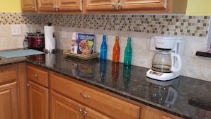 A kitchen with wooden cabinets, a slow cooker, a coffee maker, and colorful bottles on the counter.