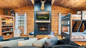 L’intérieur d’un chalet accueillant, avec une cheminée, des murs en bois, une tête de cerf décorative, un téléviseur et un lit superposé.