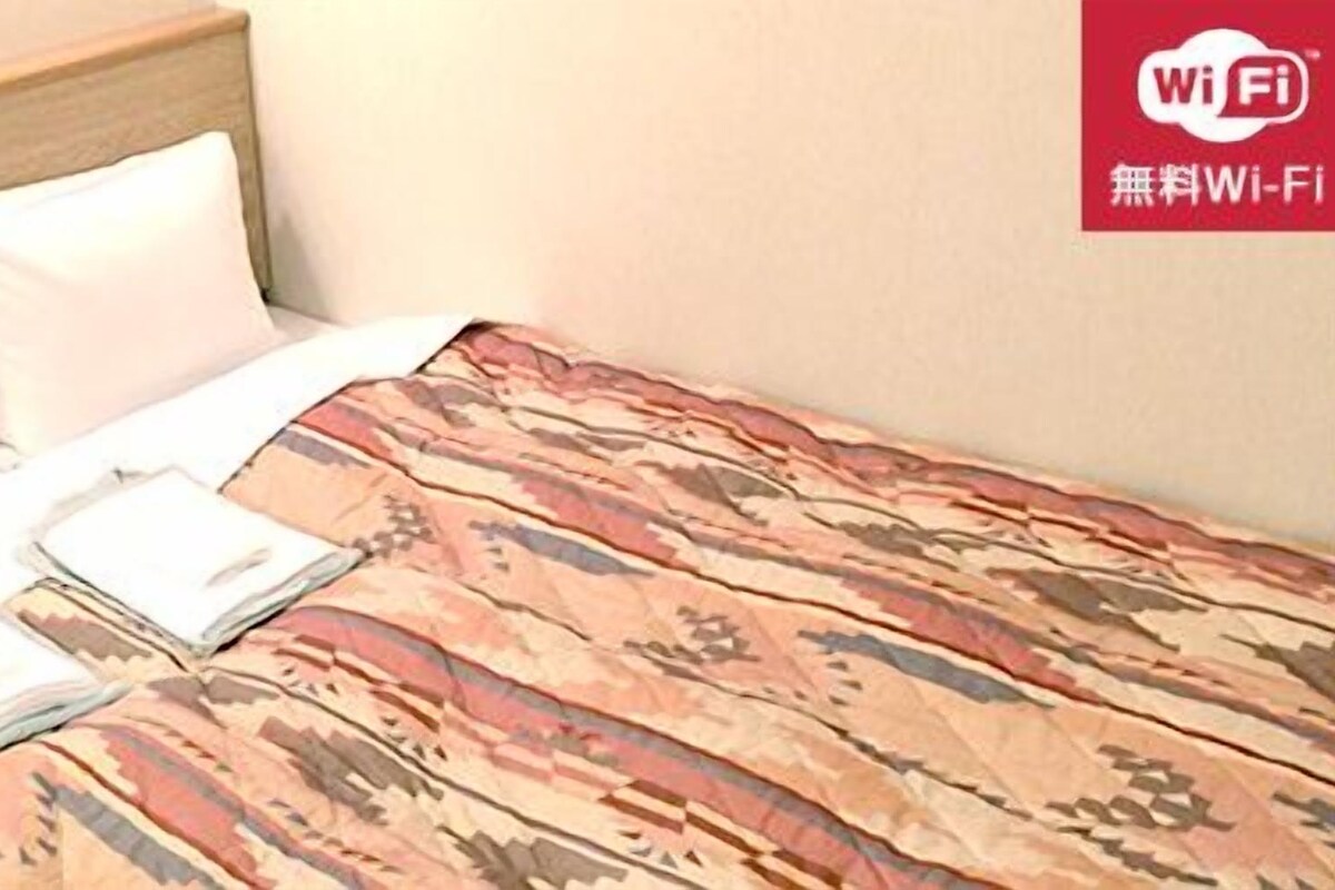 Ein Hotelzimmer mit Bett, Kissen und Decke. Ein Schild weist auf kostenloses WLAN hin.