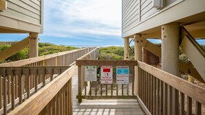 Eine Holztreppe führt zu Strandhäusern, an denen Schilder über Müll und Strudel informieren.