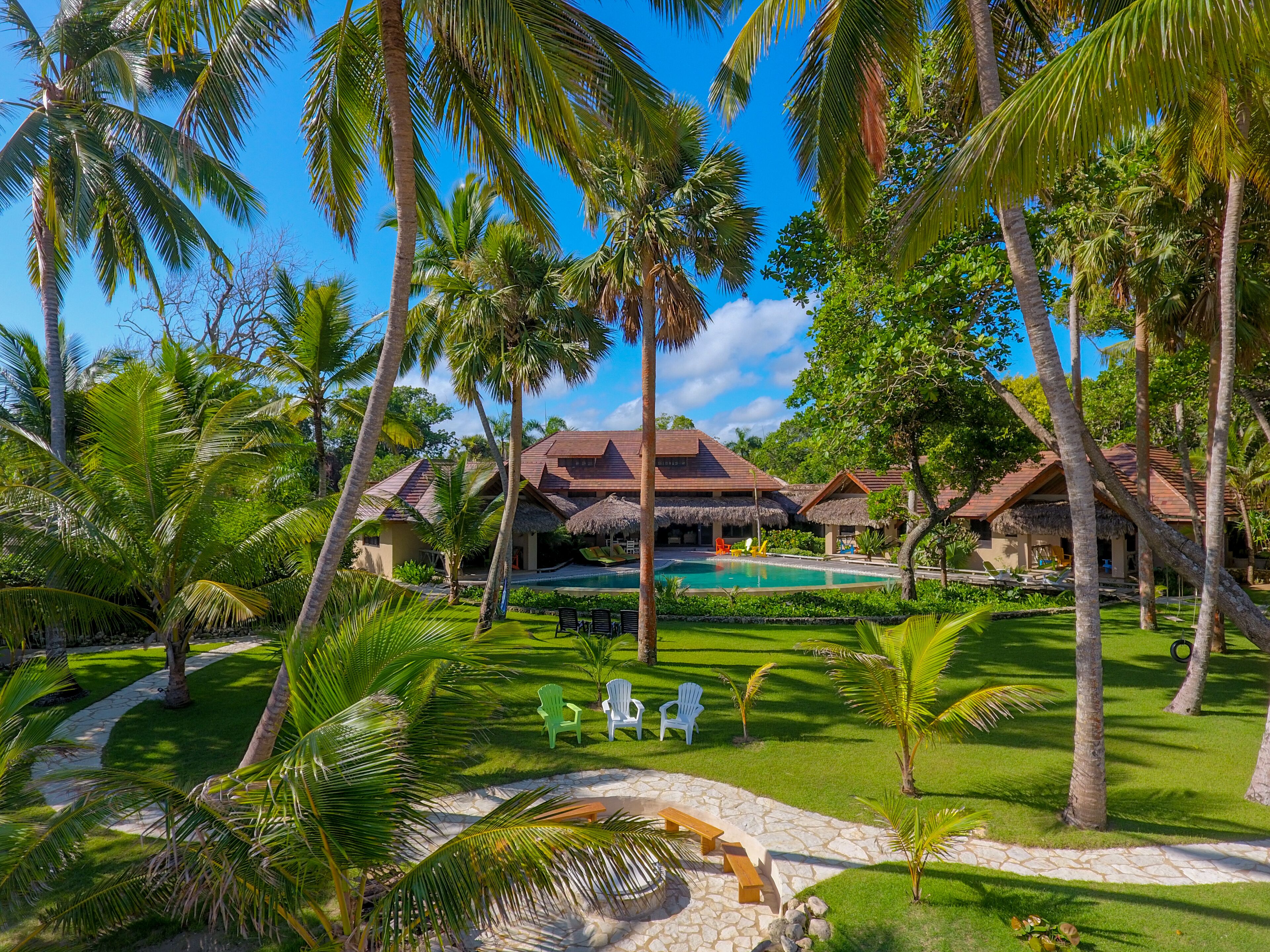 Un resort con edificios de techo de paja, piscina y exuberante vegetación.