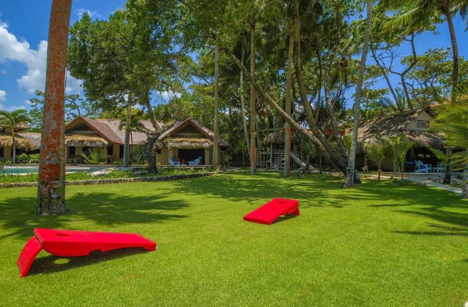 A tropical resort with thatched-roof cottages, a pool, and a well-maintained lawn.