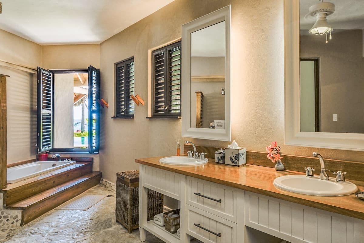 A bathroom with a bathtub, two sinks, a large mirror, and a window with shutters.