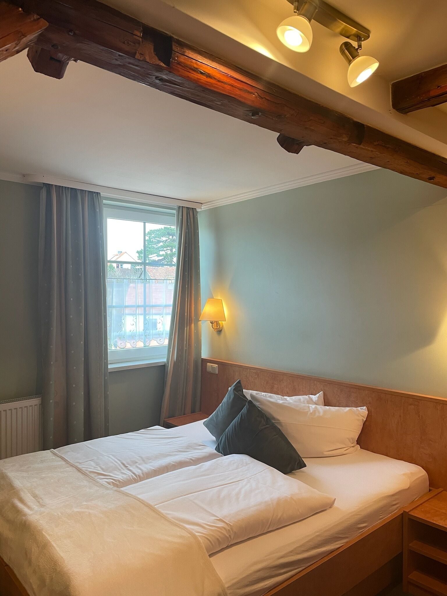 Ein Hotelzimmer mit einem Bett, einem Nachttisch, einer Lampe und einem Fenster mit Vorhängen.