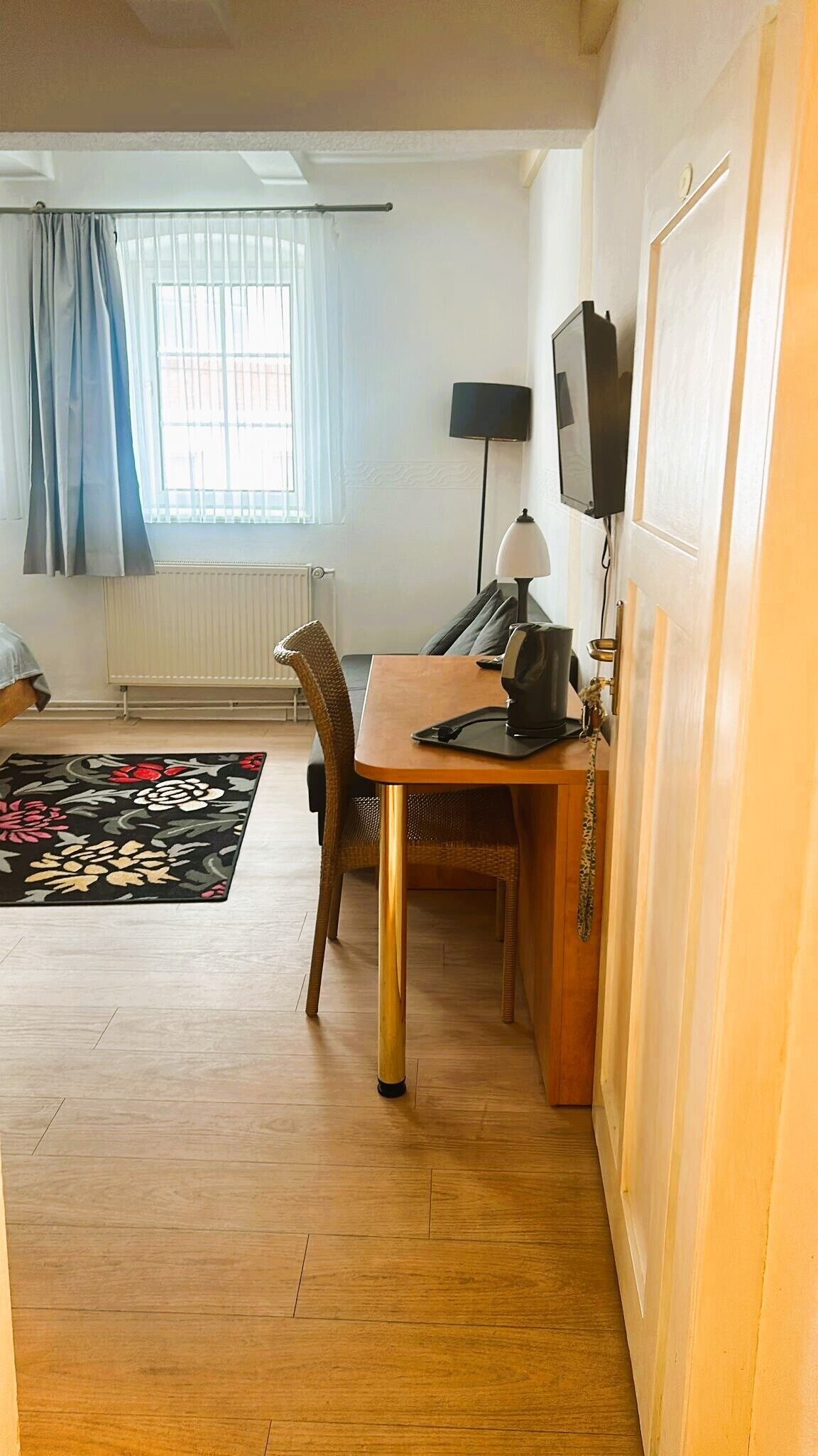 A compact room with a wooden dining table, a chair, a small black lamp, and a television mounted on the wall.