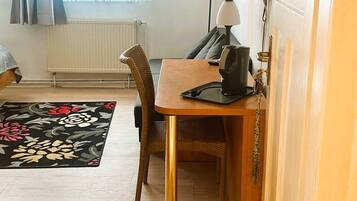 A compact room with a wooden dining table, a chair, a small black lamp, and a television mounted on the wall.