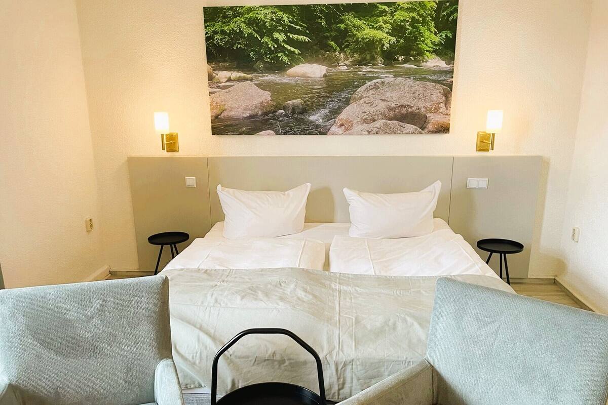 Een hotelkamer met een bed, twee nachtkastjes, een bank en een schilderij van een rivierlandschap.