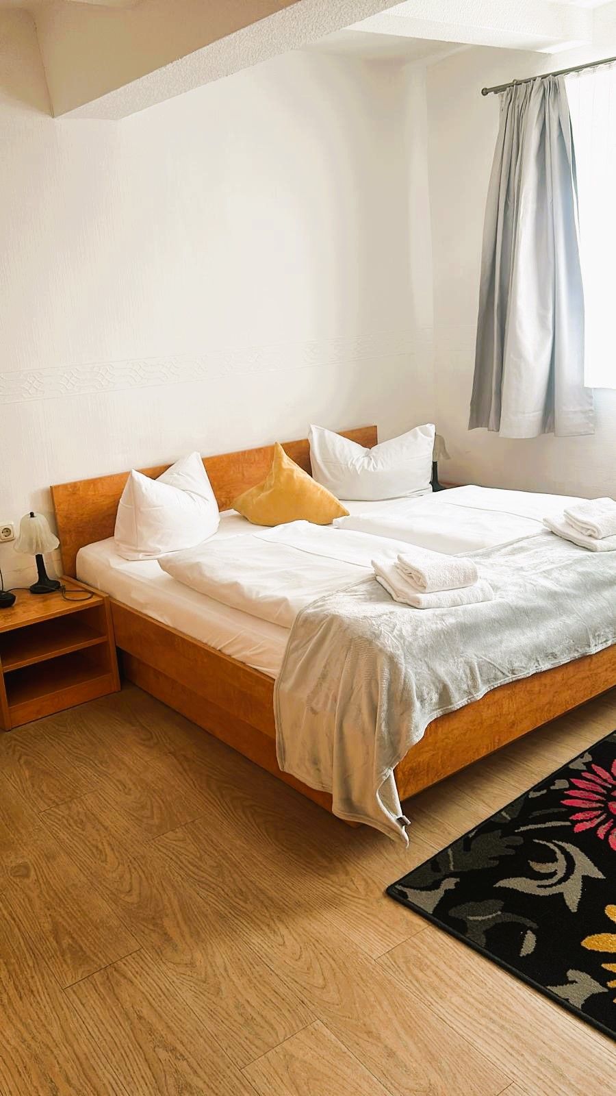 A neatly made bed with white linens, a wooden headboard, and a bedside table with a lamp.