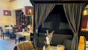 Een gezellig eetgedeelte met een ronde tafel, stoelen, een boekenkast en een zithoek met gestreepte gordijnen.