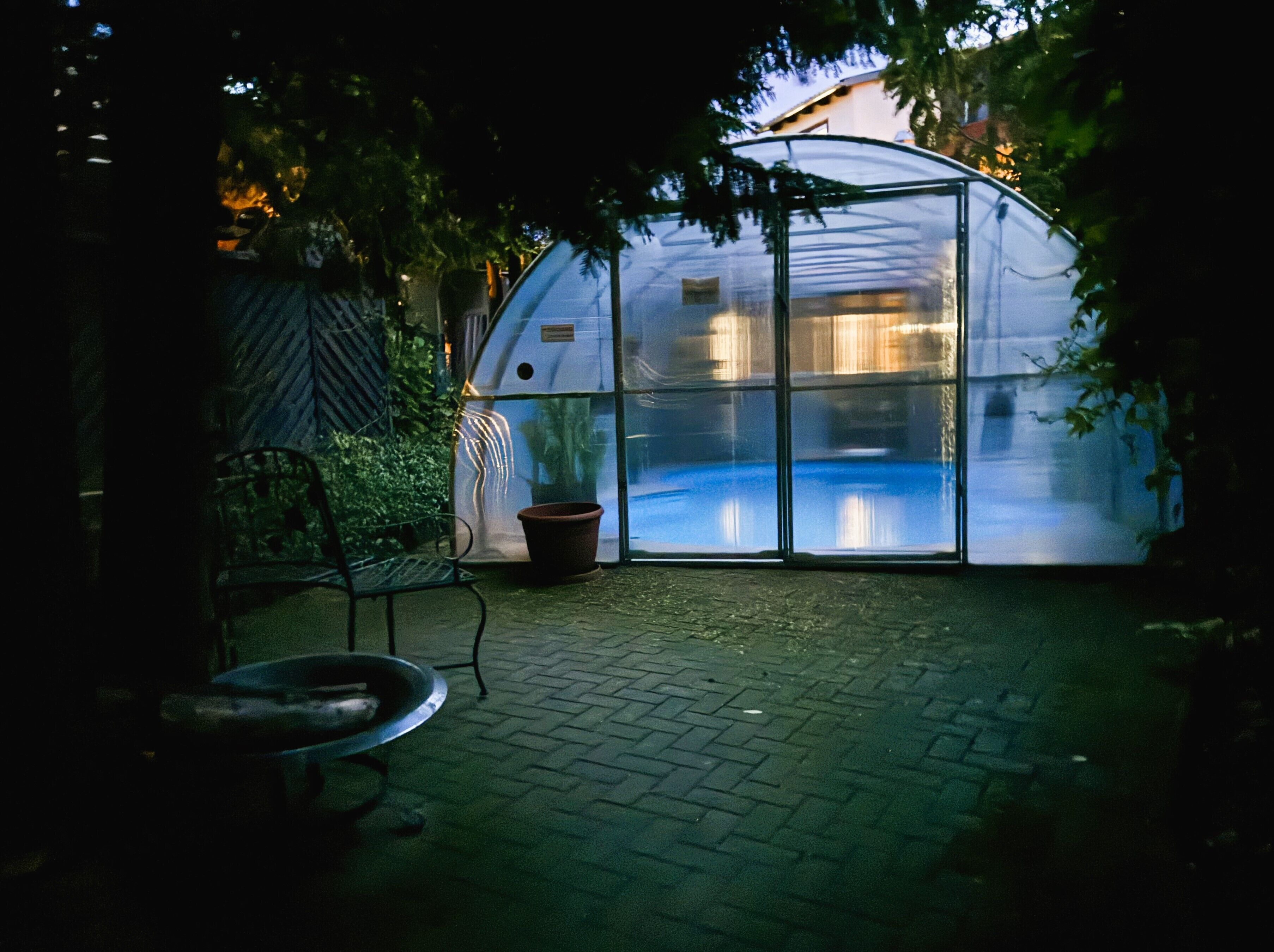 A greenhouse with a transparent roof, a metal bench, and a potted plant.
