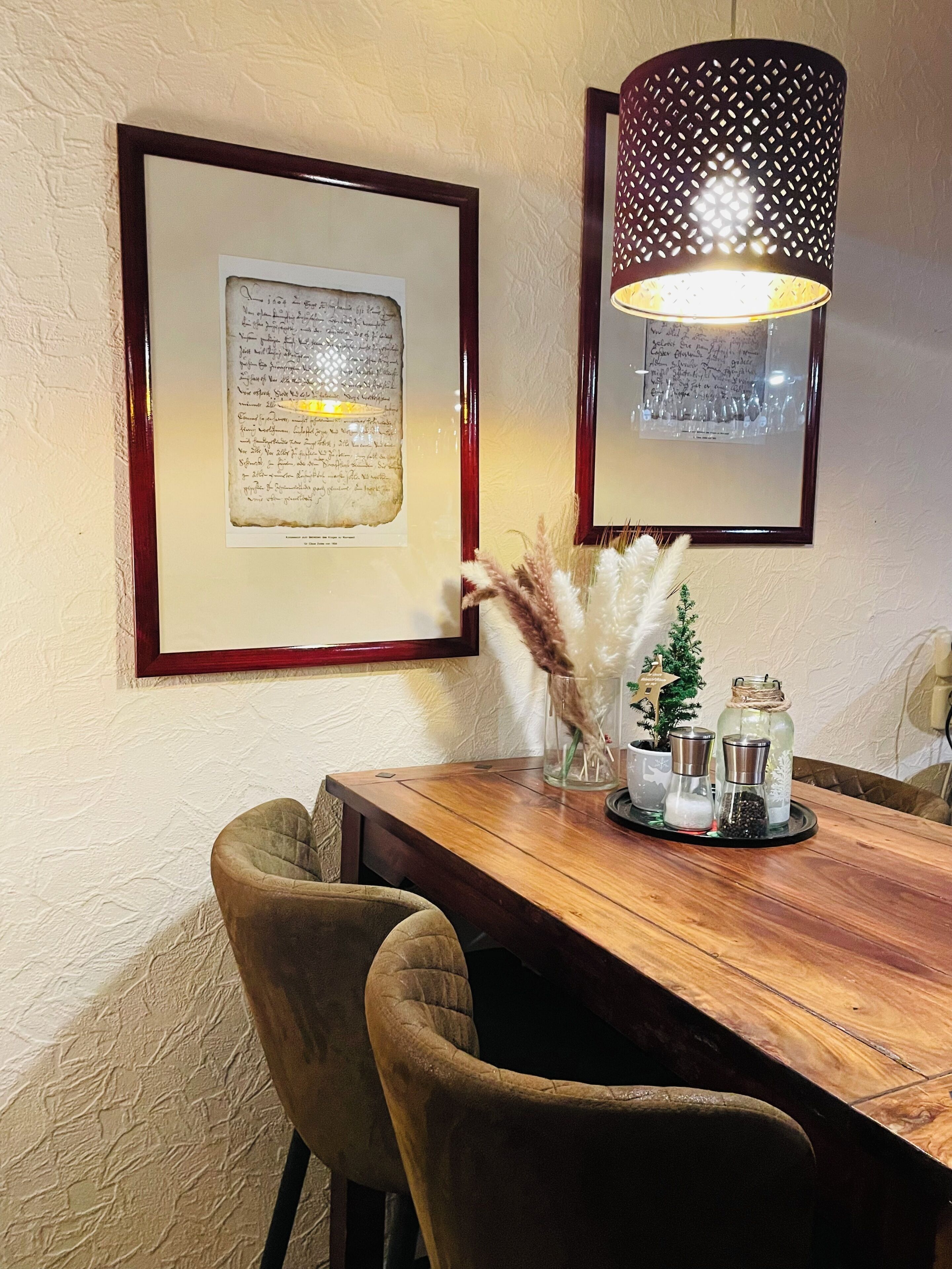 Ein Holztisch mit Stühlen, gerahmte Dokumente an der Wand, eine Zierlampe und kleine Topfpflanzen.
