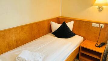 Un letto singolo con lenzuola bianche e un cuscino nero, un comodino con una lampada e un telefono.