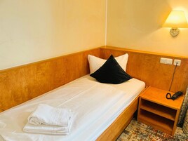 Un letto singolo con lenzuola bianche e un cuscino nero, un comodino con una lampada e un telefono.