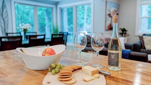 A dining table with a bowl of fruit, cheese, crackers, and a bottle of wine. - Hoopers Creek Cottage | Creekside Retreat Near Asheville + Hendersonville (Fletcher)