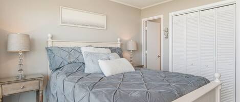 A bedroom with a bed, nightstands, a ceiling fan, a door, and a closet.
