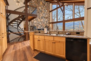 Eine Küche mit Steinwand, Holzschränken, einem integrierten Geschirrspüler und Blick ins Freie.