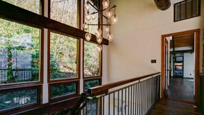 A spacious hallway with large windows, a wooden staircase, and a modern light fixture.
