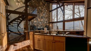 A kitchen with wooden cabinets, a stone wall, a built-in dishwasher, and a large window overlooking a mountainous landscape.