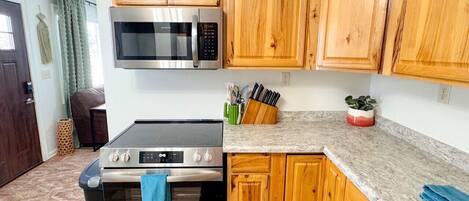 Una cocina con armarios de madera, microondas, horno y encimera con fregadero.