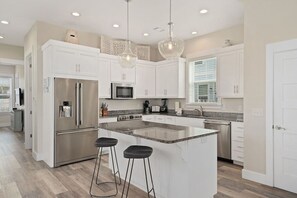 A modern kitchen with white cabinetry, stainless steel appliances, and a central island with bar stools.