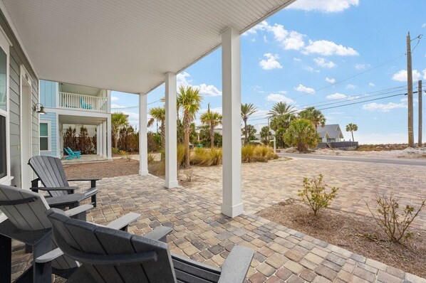 A covered outdoor area with Adirondack chairs, a brick patio, and a view of a house with a balcony.