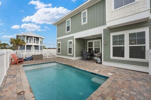 A two-story house with a swimming pool, a covered patio, and a white fence.
