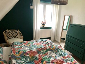 Une chambre à coucher comprenant un lit, une chaise, une commode, une fenêtre avec des rideaux et un luminaire suspendu.