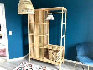 Een kamer met een blauwe wand, een houten vloer, een blauwe stoel, een rieten lamp en een houten kast met planken.