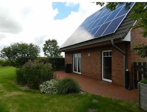 A house with a solar panel roof, brick walls, and a small garden.