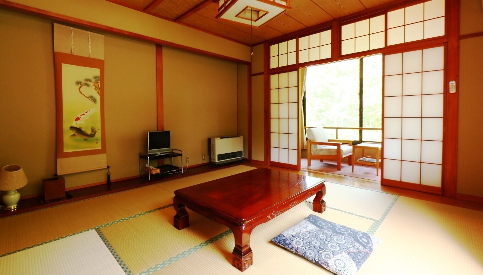 Una habitación tradicional japonesa con suelo de tatami, una mesa de madera, un televisor y puertas correderas.
