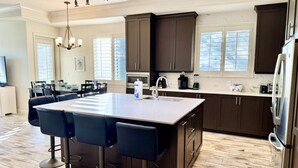 A modern kitchen with a large island, dark cabinetry, and a dining area with bar stools. - Golfers` Paradise. Large Townhouse By 1st Hole In Private Gated Community (Gulf Shores)