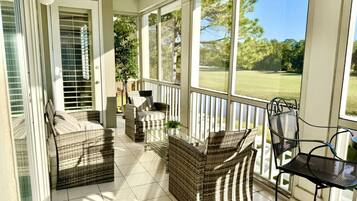 A covered porch with wicker furniture, a glass railing, and a view of a golf course.