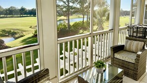 A room with large windows, wicker furniture, and a view of a golf course. - Golfers` Paradise. Large Townhouse By 1st Hole In Private Gated Community (Gulf Shores)