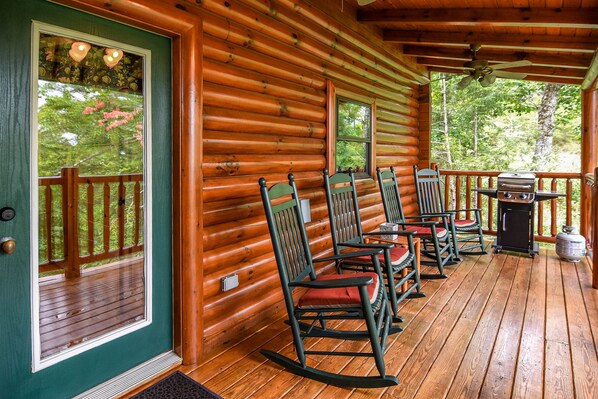 A wooden cabin with a porch featuring rocking chairs and a grill.
