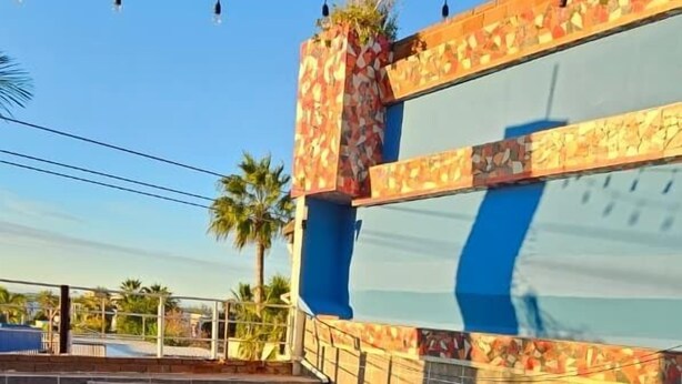 A swimming pool with a tiled edge, a decorative wall with a floral pattern, and a clear blue sky in the background. - Hotel Mágico del Mar (La Paz)