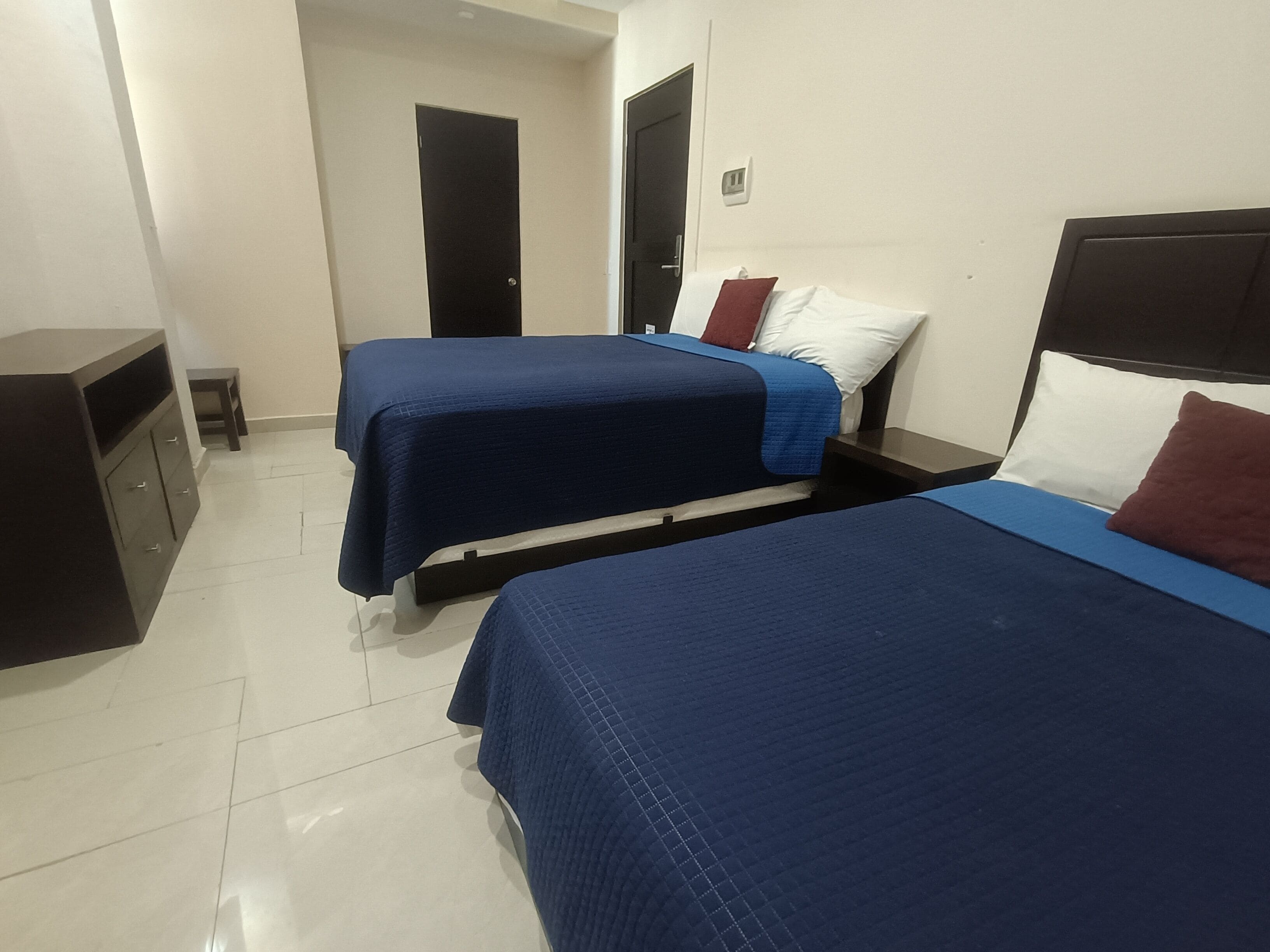 A hotel room with two beds, a small desk, and a wardrobe.