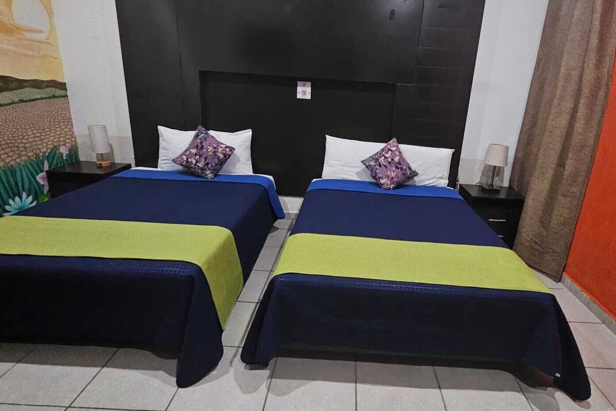 A hotel room with two beds, each with a blue and yellow bedspread, white pillows, and a black headboard.
