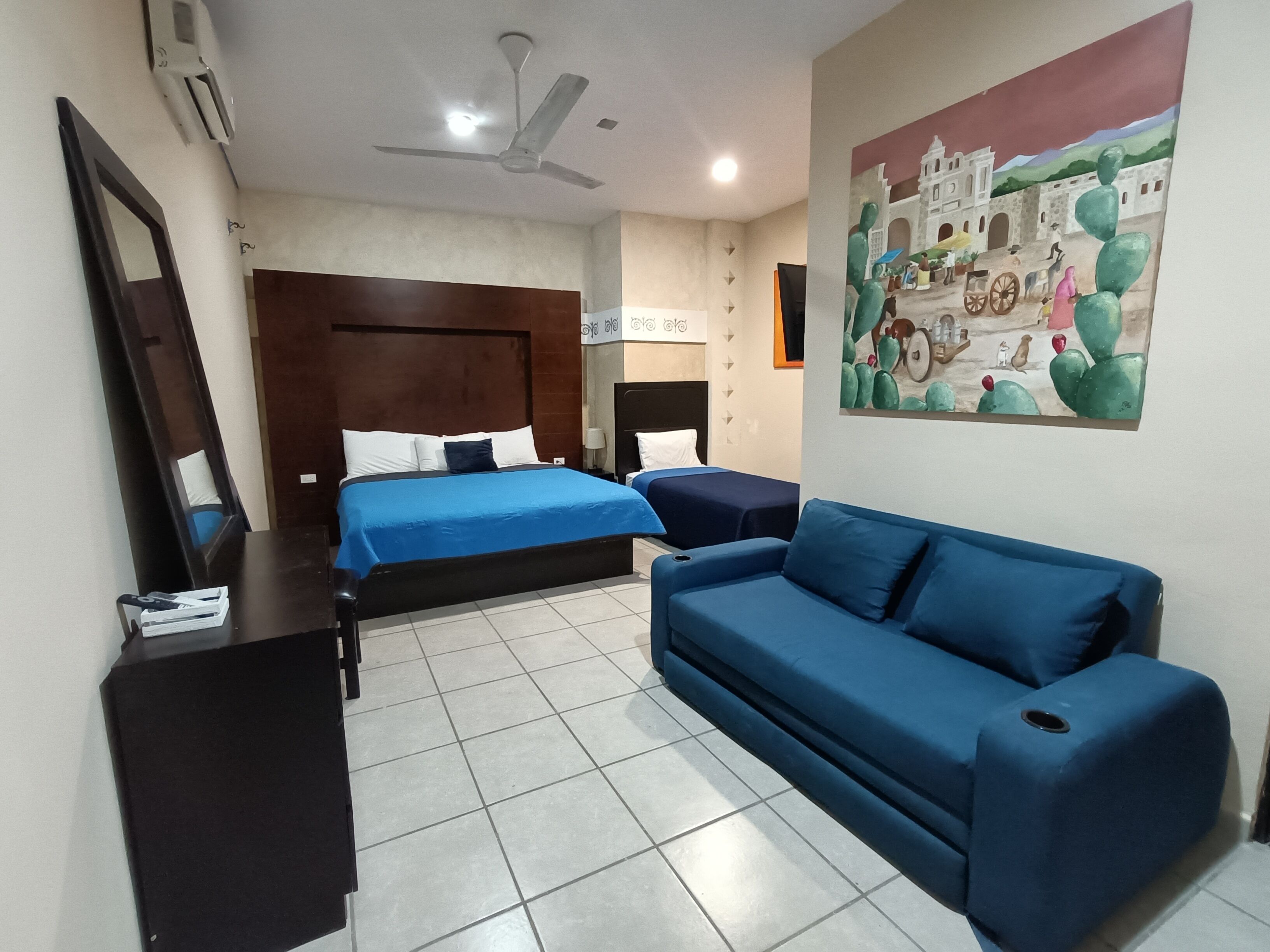 A hotel room with a bed, a sofa, a desk, and a ceiling fan.