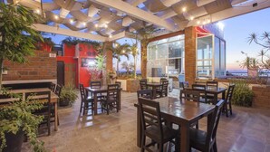 An outdoor patio with tables and chairs, a brick wall, and a view of the ocean. - Hotel Mágico del Mar (La Paz)