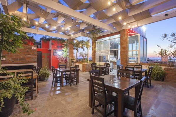 An outdoor patio with tables and chairs, a brick wall, and a view of the ocean. - Hotel Mágico del Mar (La Paz)