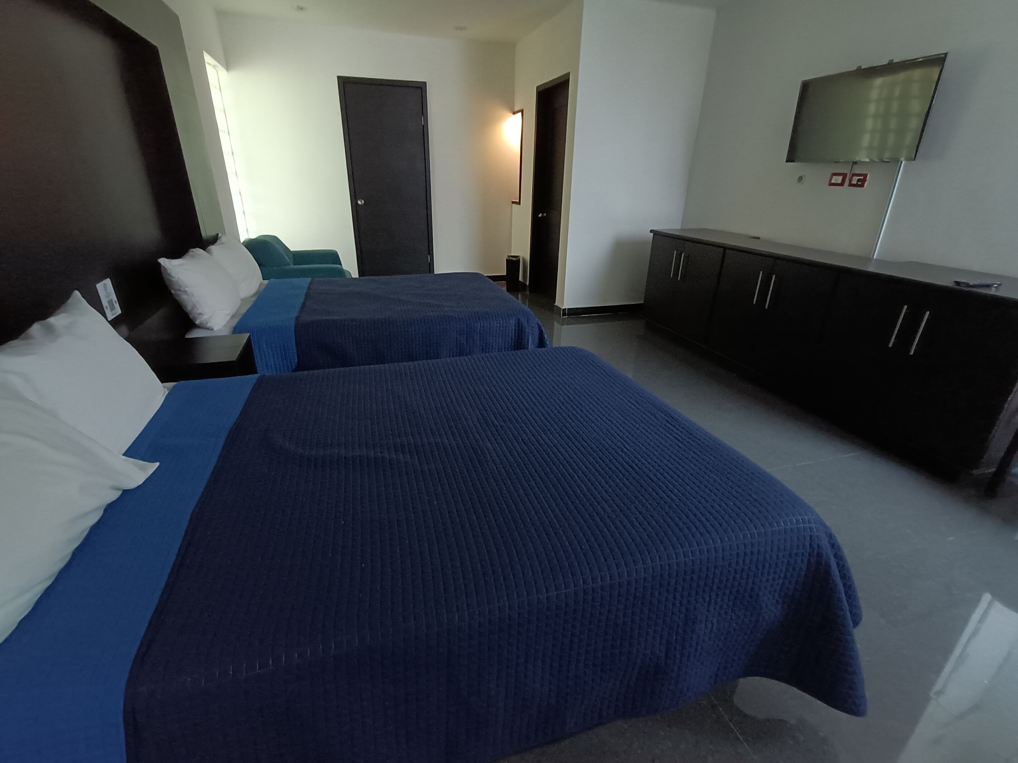 Una camera d'albergo con due letti, una televisione a parete e un armadio scuro.