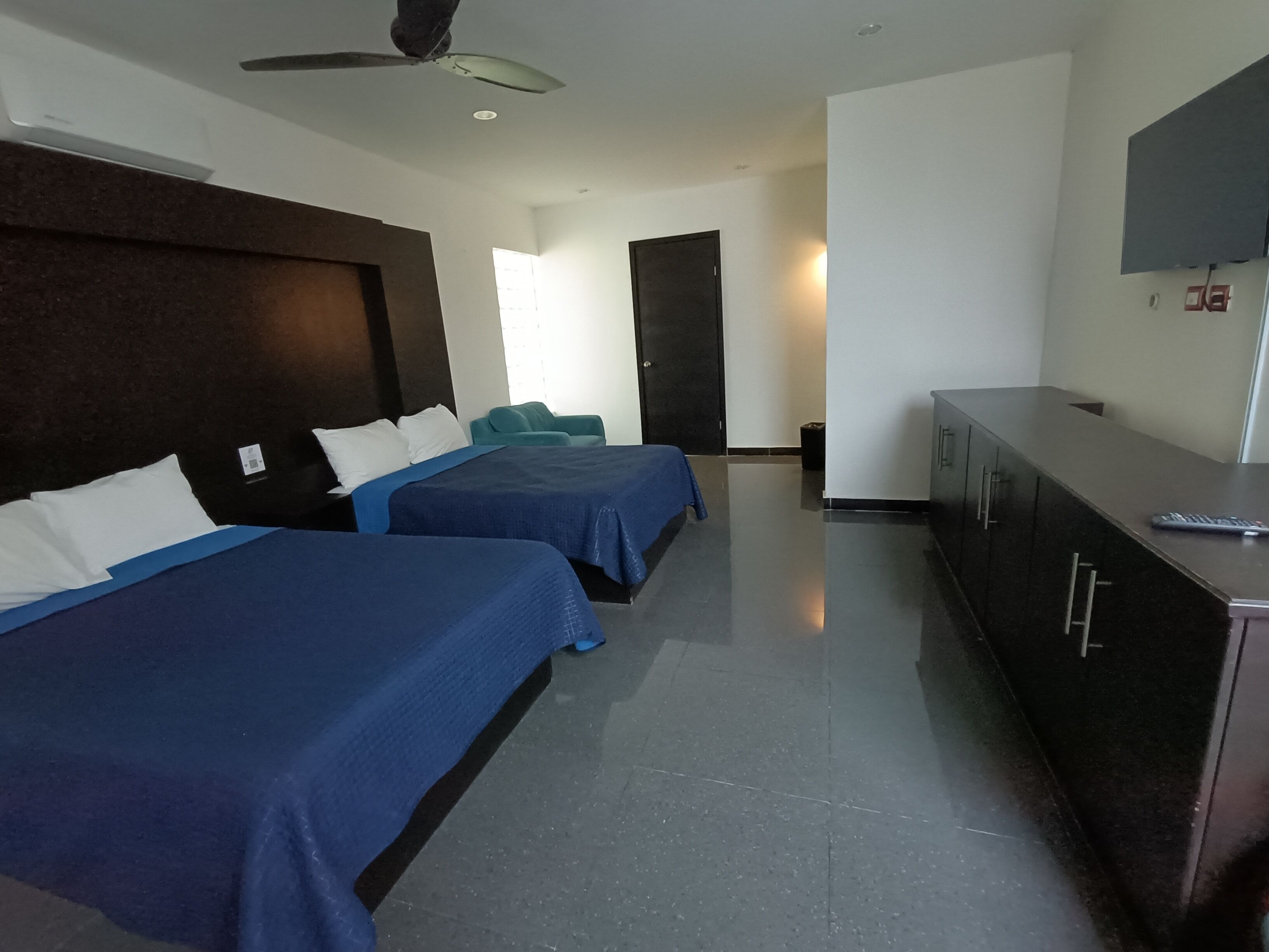 A hotel room with two beds, a desk, a television, and a ceiling fan.