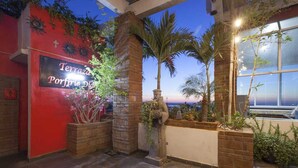A hotel entrance with a red wall, a sign reading "Terrazas Porfiros Diaz," and a view of the ocean at dusk. - Hotel Mágico del Mar (La Paz)