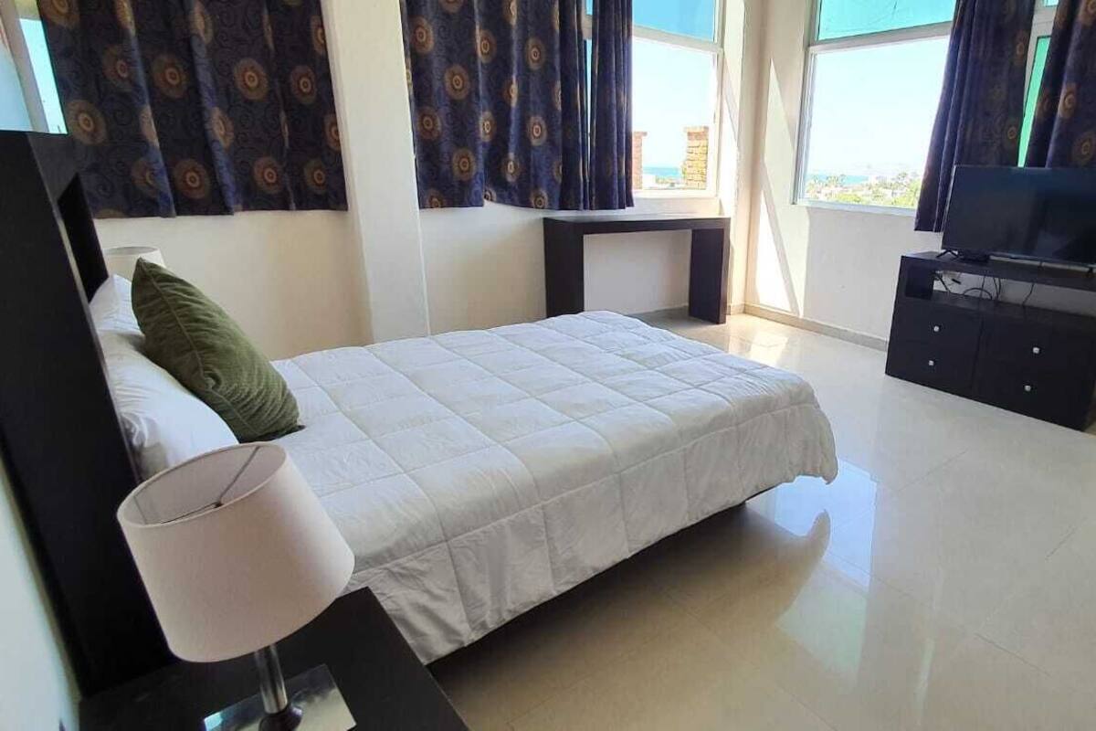 A bedroom with a bed, a bedside table, a TV, and curtains.