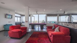 A modern living room with red sofas, a pool table, and large windows offering a view of the sea. - Hotel Mágico del Mar (La Paz)