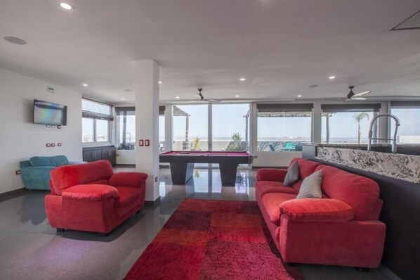 A modern living room with red sofas, a pool table, and large windows offering a view of the sea. - Hotel Mágico del Mar (La Paz)