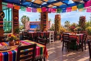 An outdoor dining area with tables covered in colorful tablecloths, surrounded by brick walls and potted plants. - Hotel Mágico del Mar (La Paz)