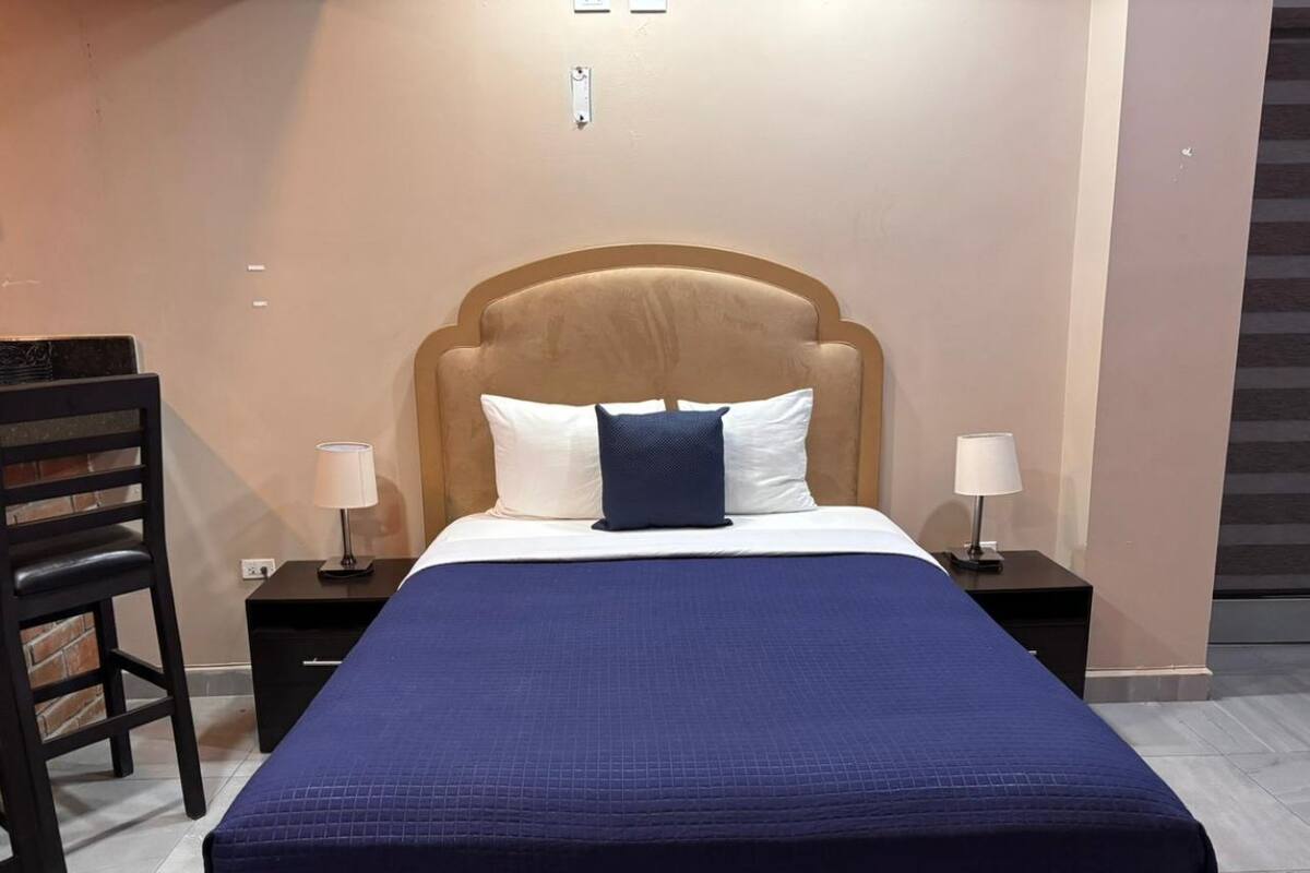 A bedroom with a bed, two nightstands, a chair, and a wall-mounted light fixture.